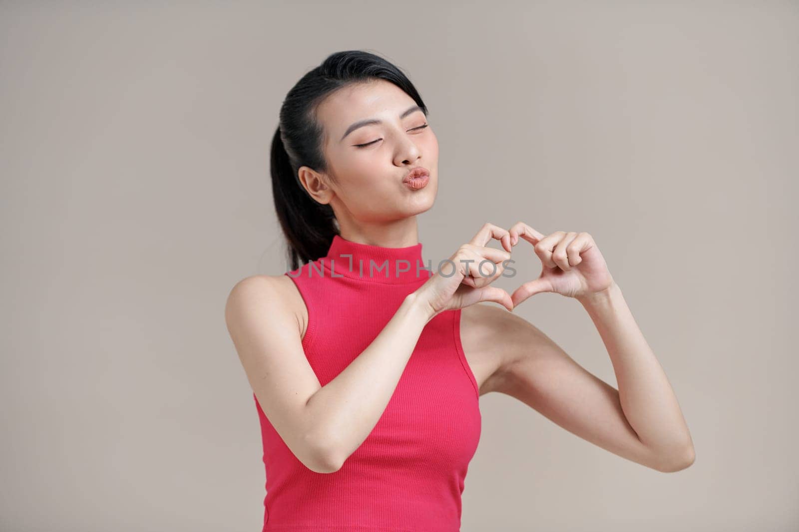 Pretty romantic young asian woman making a heart gesture with her fingers in front of her chest 