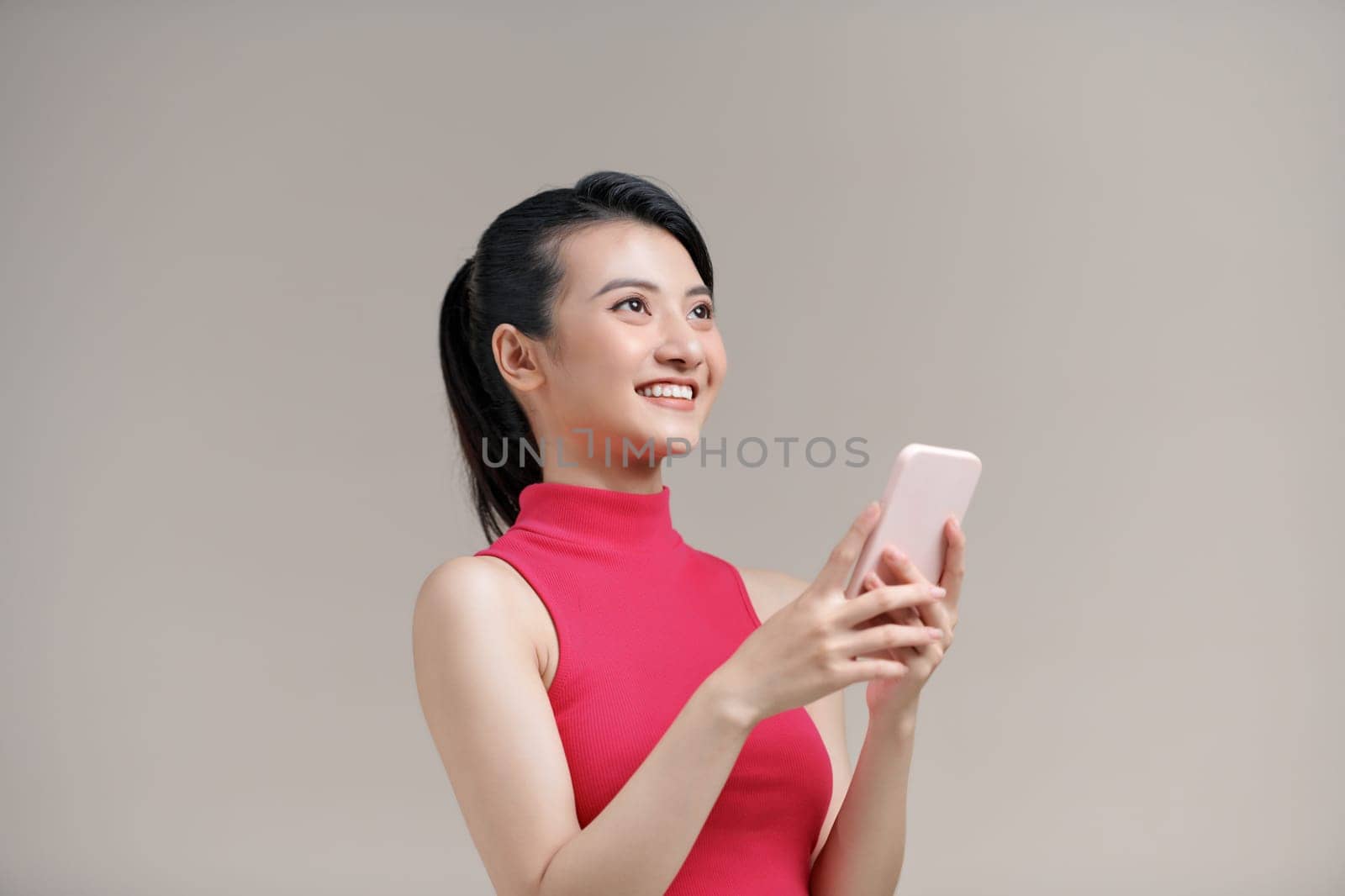 Asian girl using smartphone with wireless connection over beige studio background by makidotvn