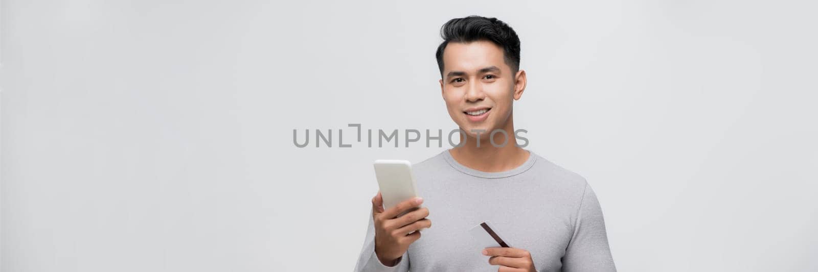 Young asian smiling attractive man hold mobile cell phone credit bank card shopping online. Panorama by makidotvn