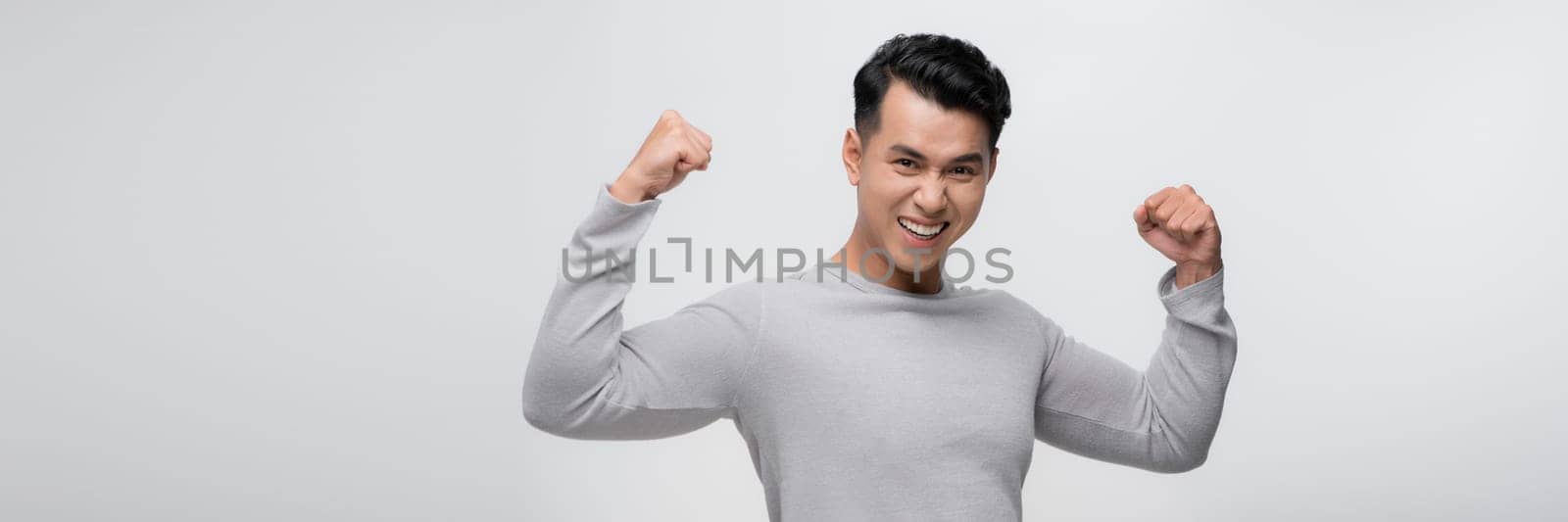 Young handsome asian man over white backgroundshowing arms muscles smiling proud. by makidotvn