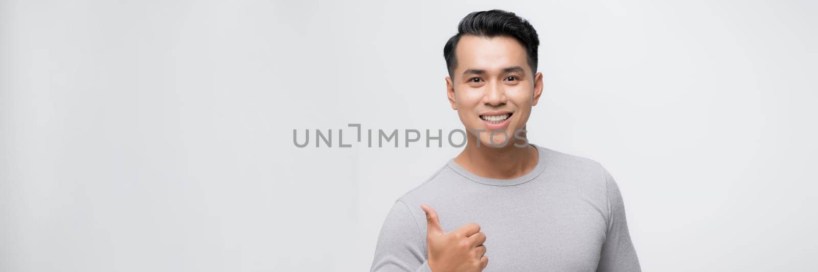 Young handsome asian man over white banner background doing happy thumbs up gesture with hand.