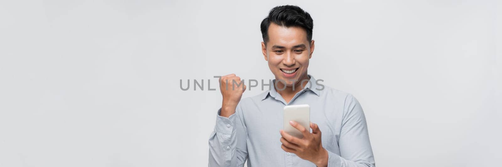  Excited asian millennial man isolated on  white background look at smartphone happy get good text message by makidotvn