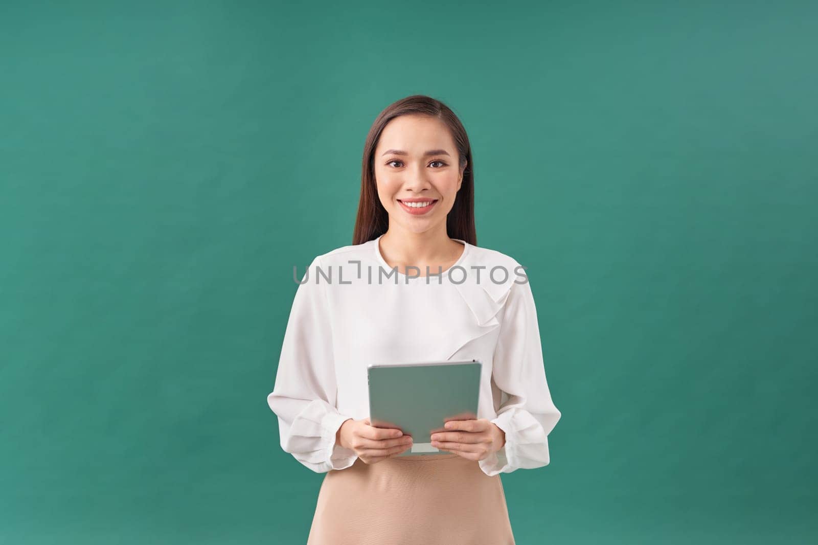 Smiling attractive businesswoman wearing formal wear holding tablet device on green background