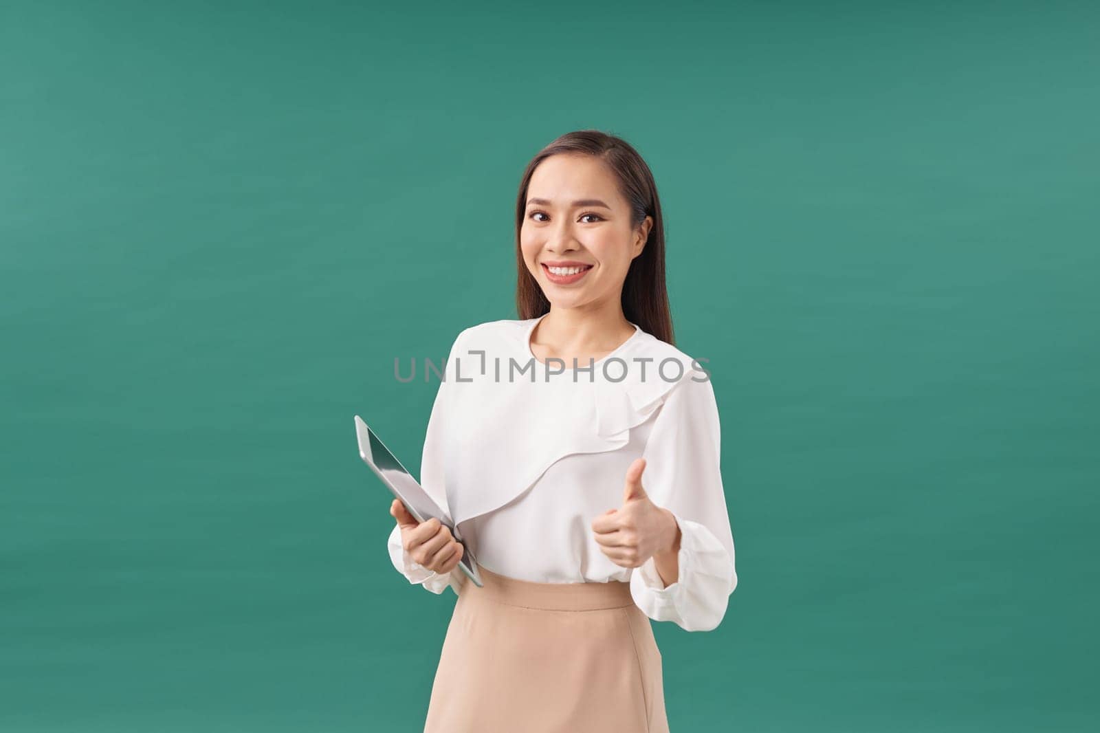 Smiling attractive businesswoman wearing formal wear holding tablet device on green background by makidotvn