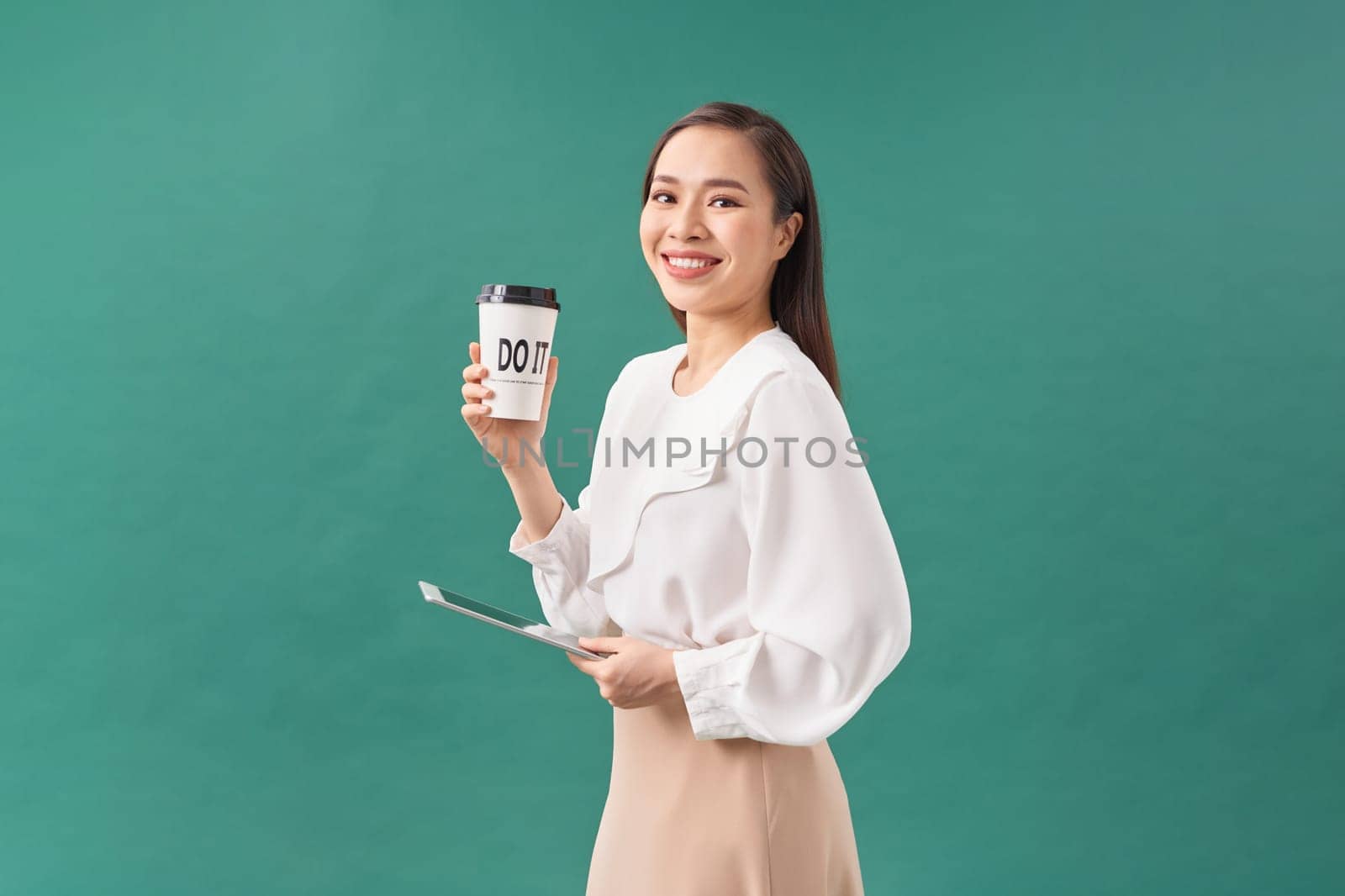 young woman holding digital tablet and paper cup isolated on green by makidotvn