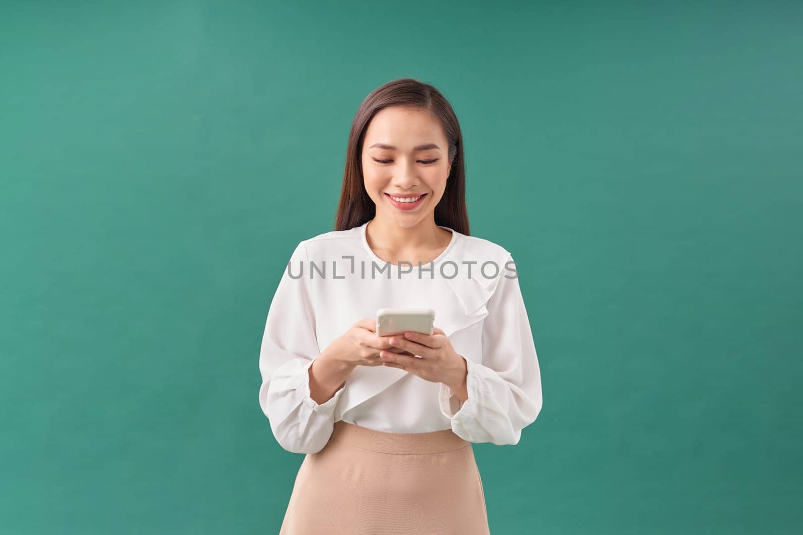 Portrait of a smiling casual woman holding smartphone over green background