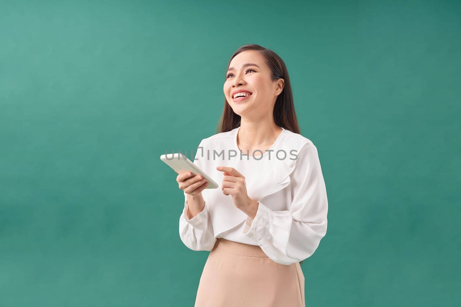 Portrait of a happy asian businesswoman using mobile phone isolated over green background