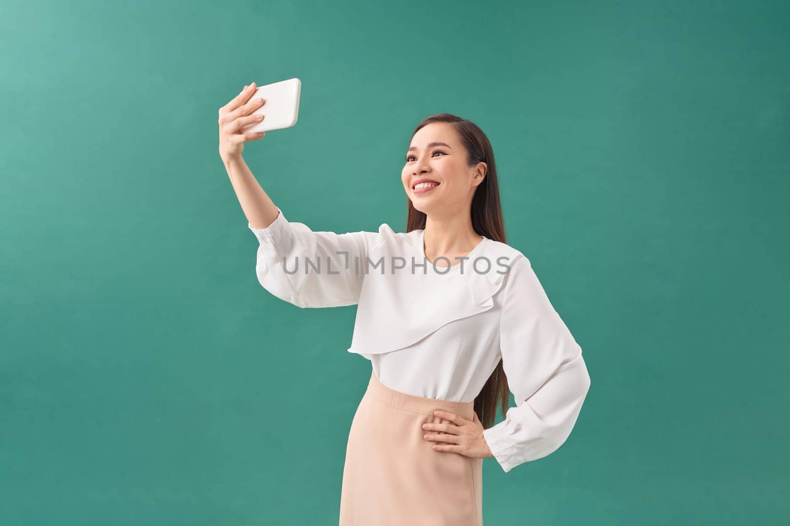 Smiling young girl making selfie photo on smartphone over green background