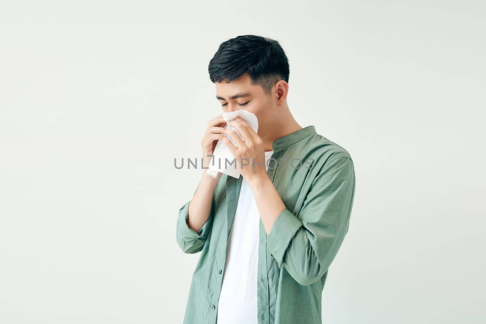 Young man wiping his nose with a tissue on white background by makidotvn