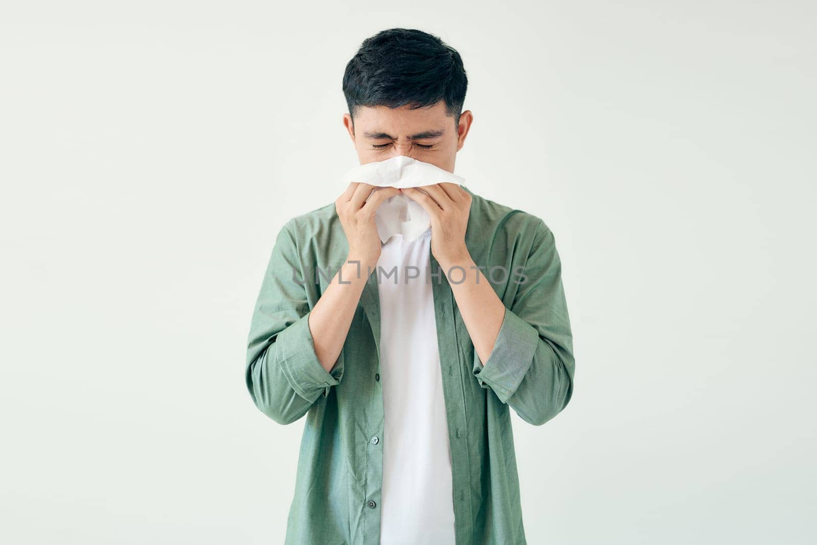 Young man wiping his nose with a tissue on white background