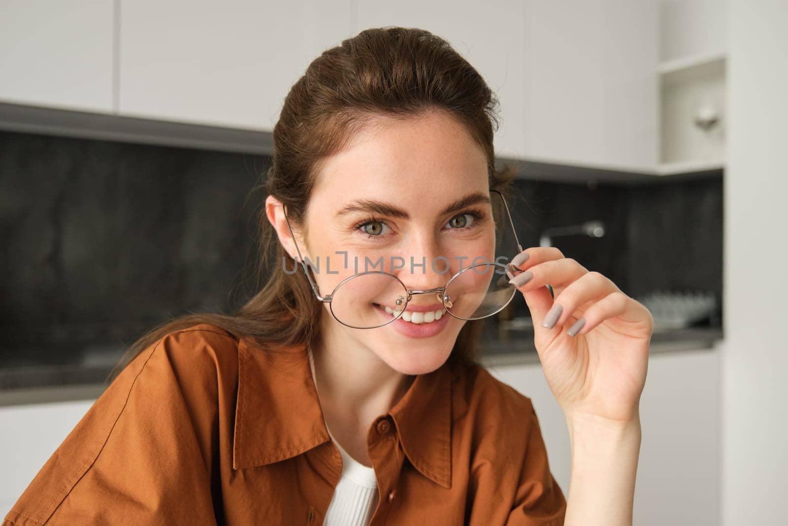 Close up portrait of carefree woman in glasses, sitting at home in kitchen, smiling and looking happy.