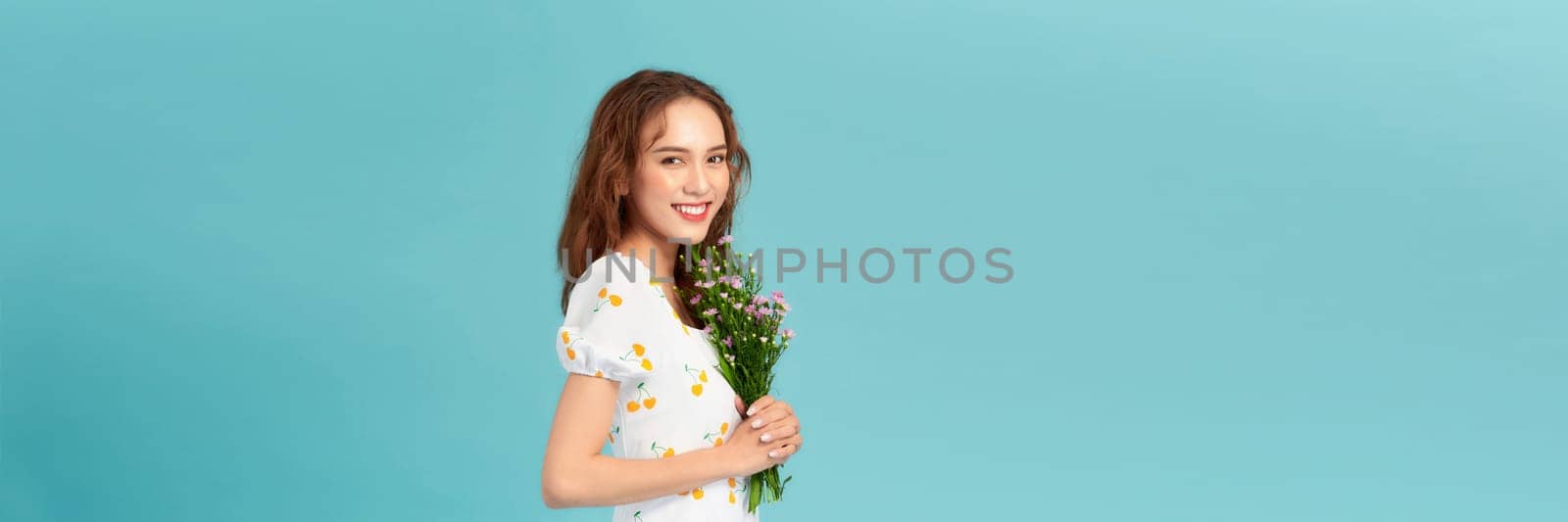 A beautiful young asian woman posing isolated over blue background holding flowers. by makidotvn