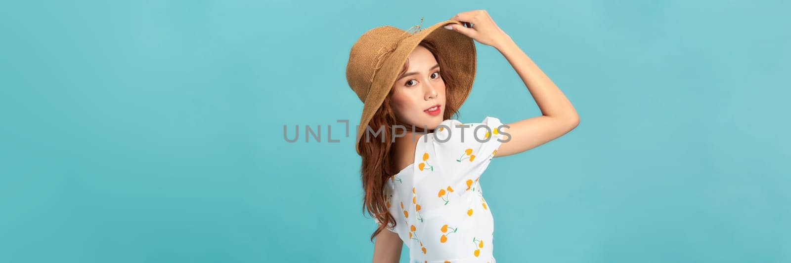 Cheerful young asian woman in summer dress and straw hat isolated on blue background.