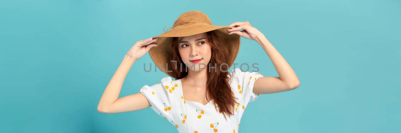 Beautiful smiling young woman in summer straw hat isolated on pastel blue background. 
