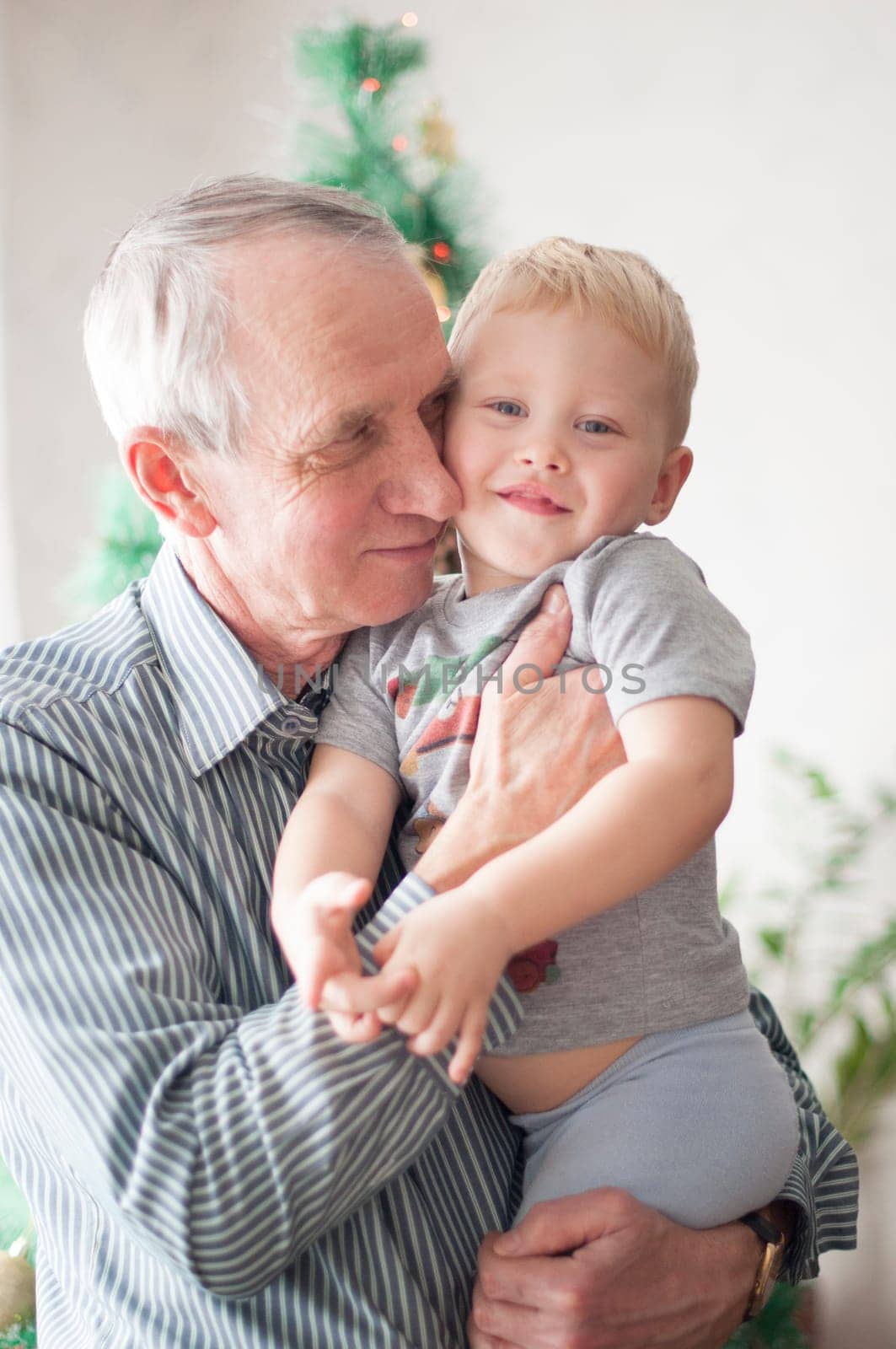 sentimental old man holding a small child in his arms at Christmas in front of a decorated Christmas tree in the grandparents house, High quality photo