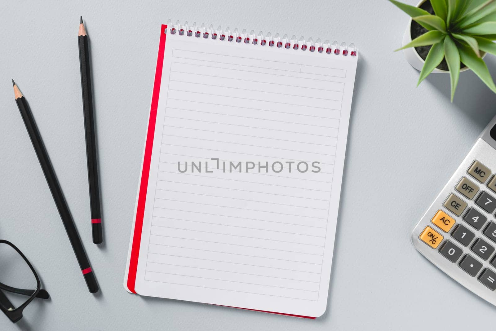 Top view of calculator, glasses, pen and green plant on grey office desk by Sonat