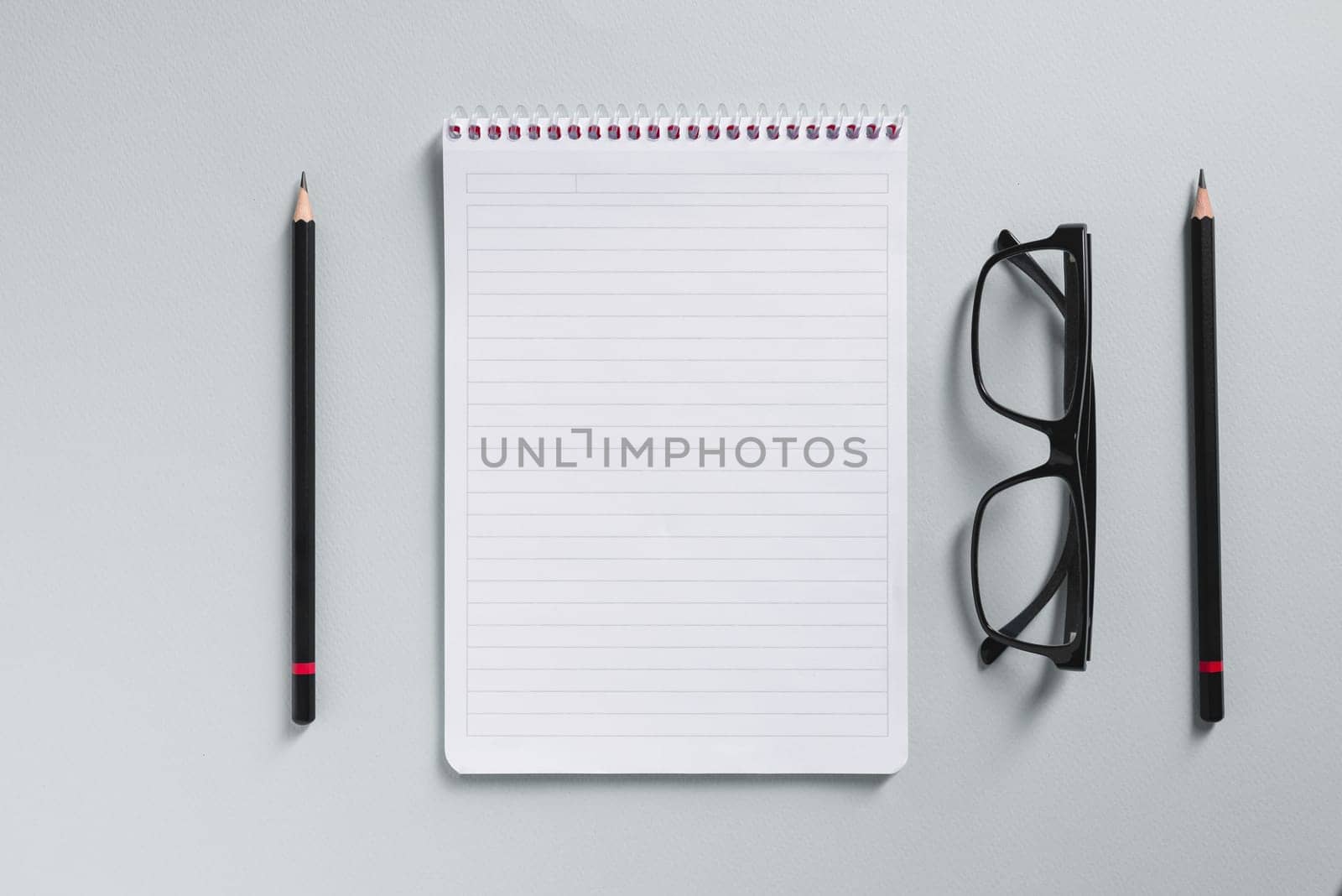 Top view of empty notebook, glasses and pen on grey office desk by Sonat