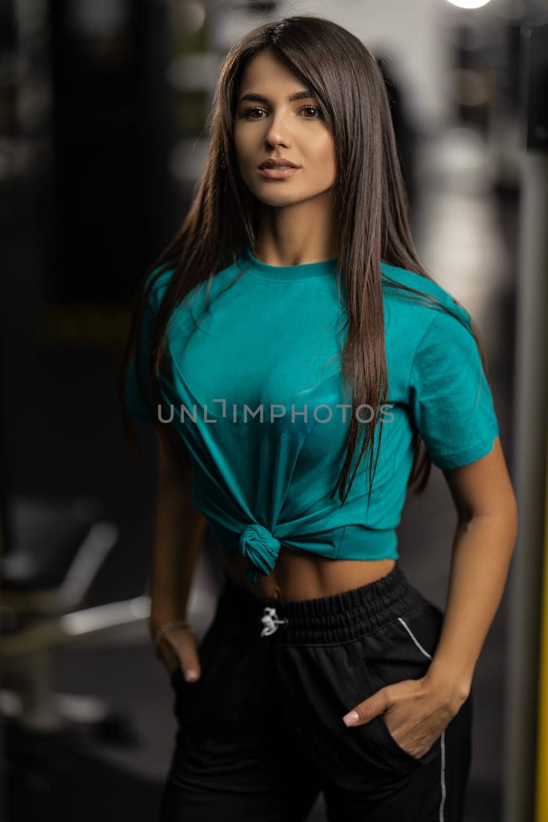 Sexy young woman fitness model with sexy abs posing in the gym with her hands in her pants pockets. Healthy athletic female body in modern sportswear