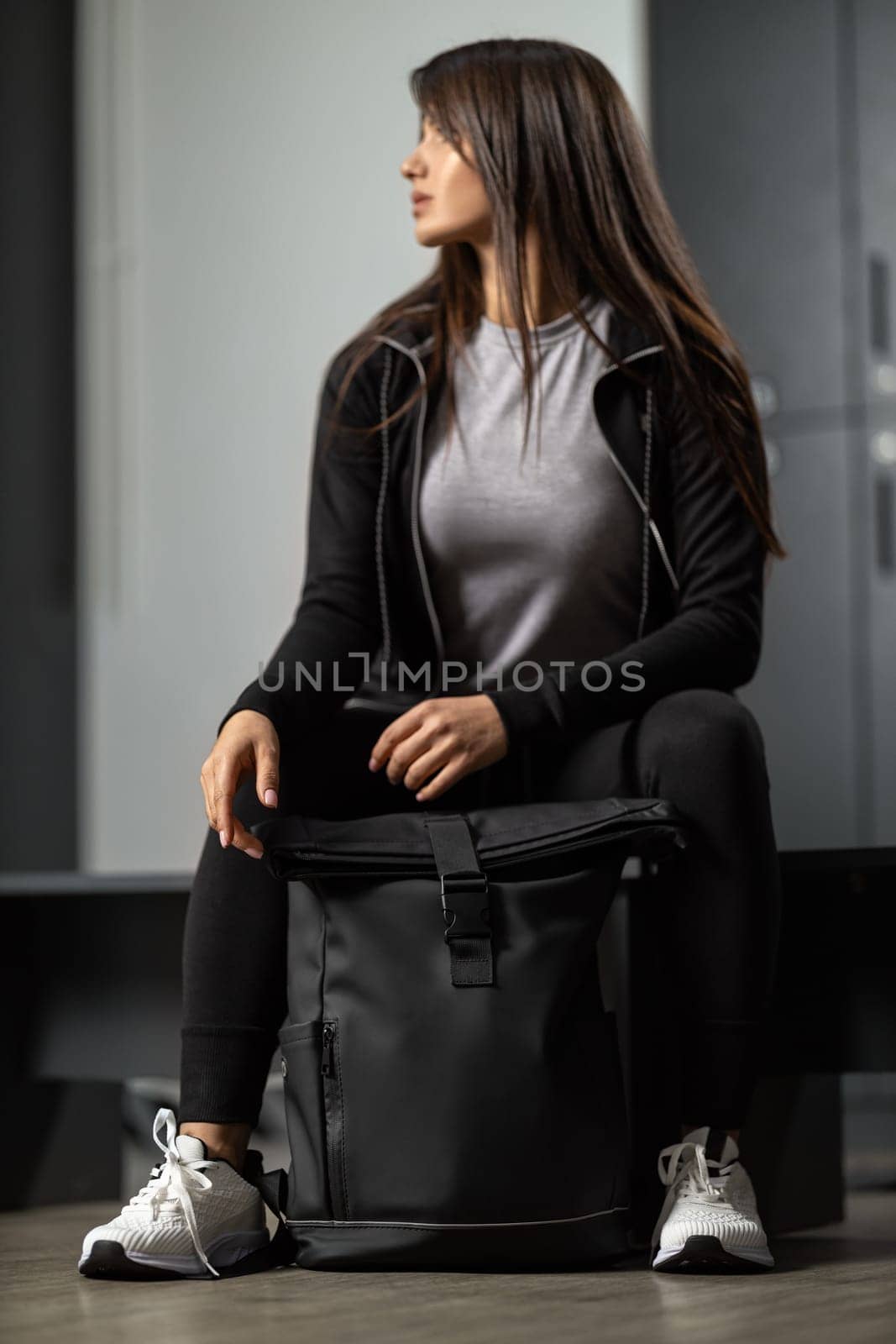 Beautiful fit brunette girl in a black tracksuit holding a sports backpack by but_photo