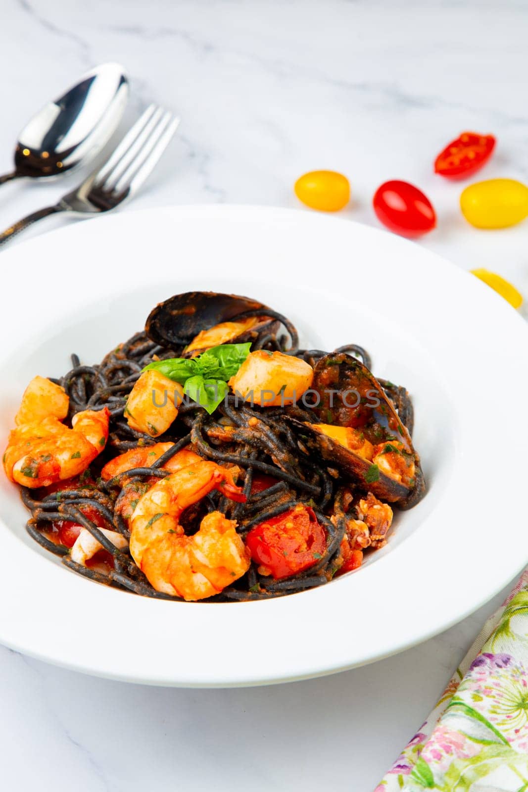 black noodles with mussels, shrimp, tomatoes and herbs side view by tewolf