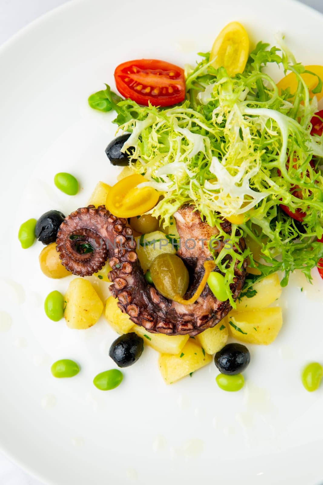 salad with olives, herbs, cherry tomatoes, potatoes and octopus tentacles top view by tewolf