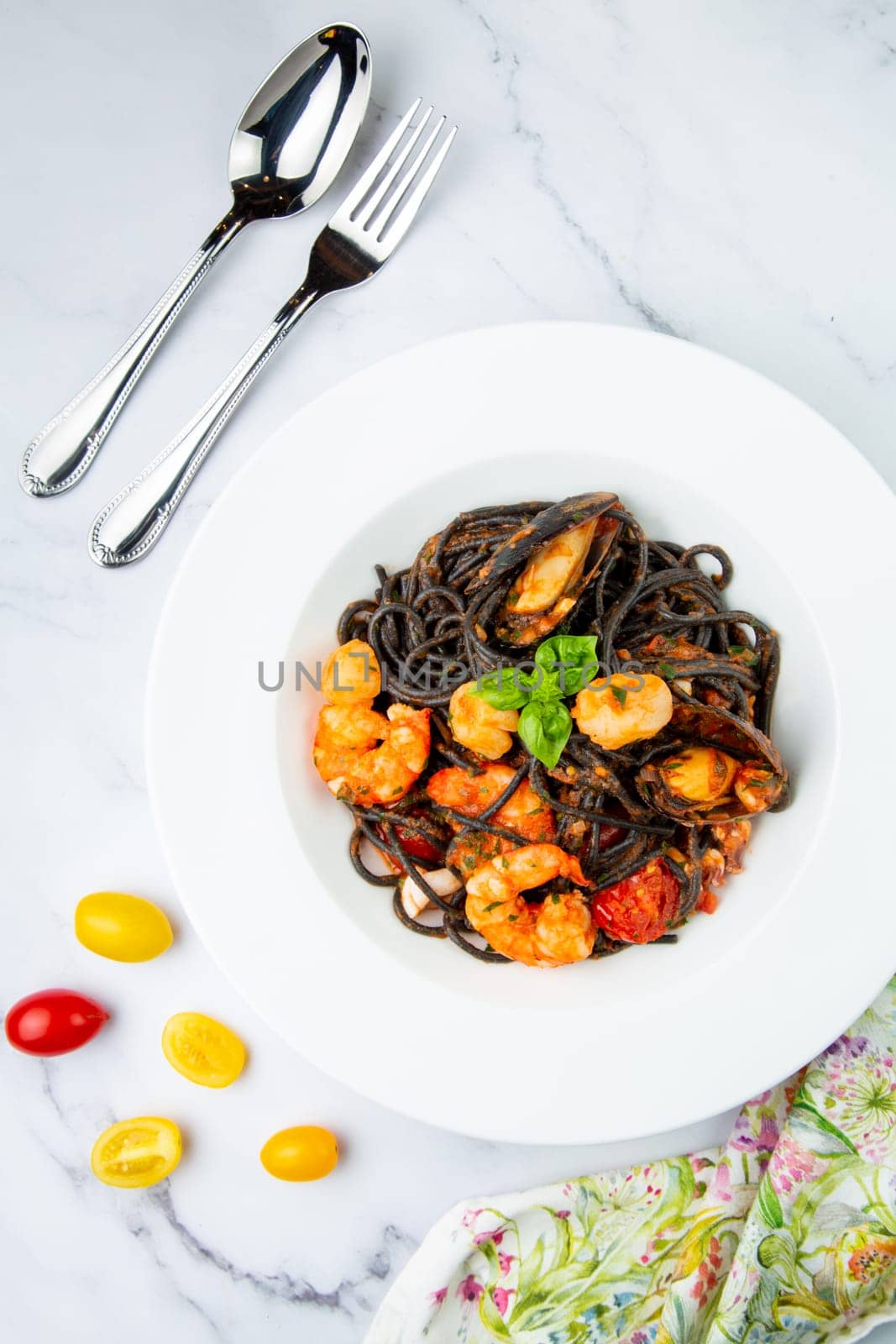 black noodles with mussels, shrimp, tomatoes and herbs side view by tewolf