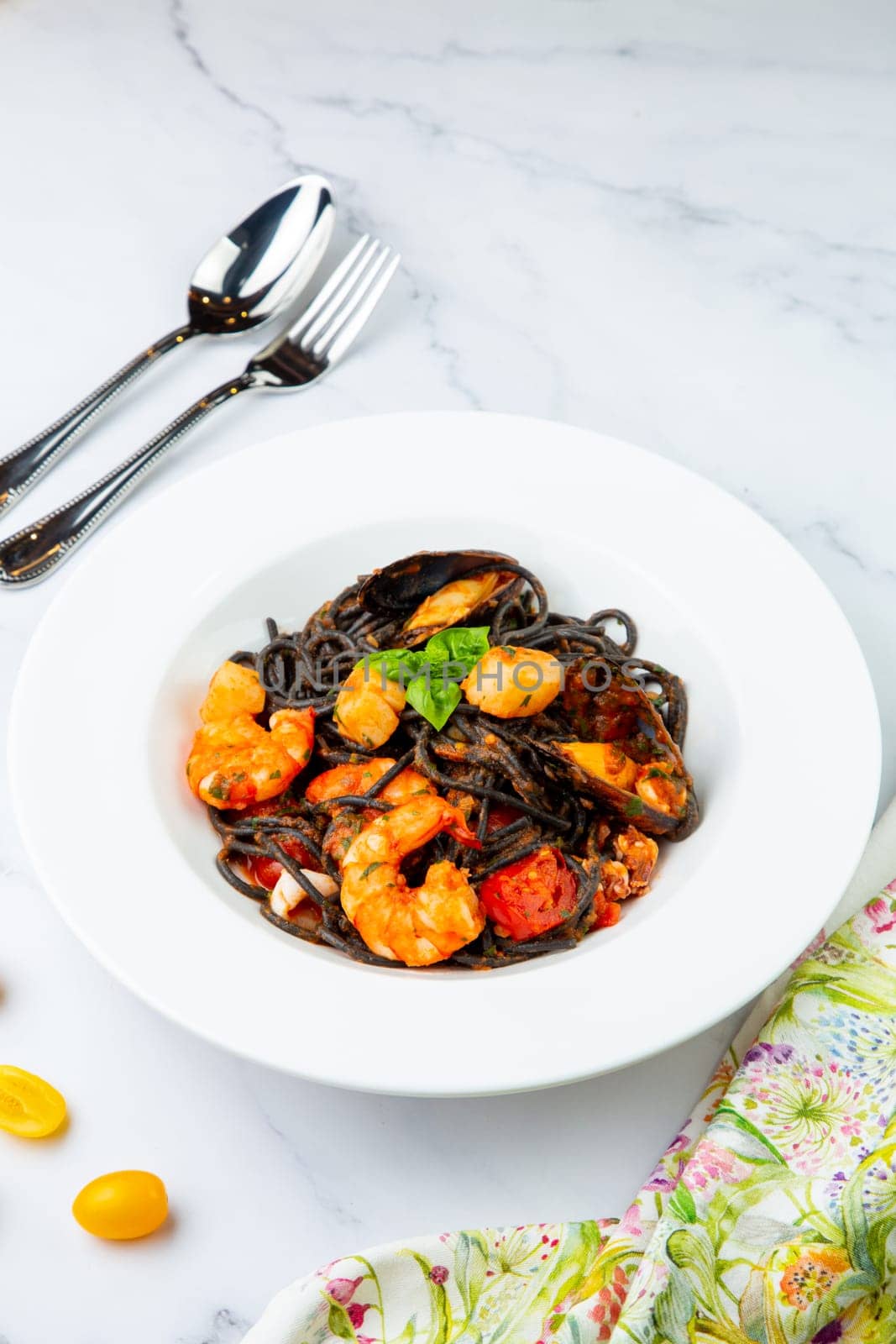 black noodles with mussels, shrimp, tomatoes and herbs side view by tewolf