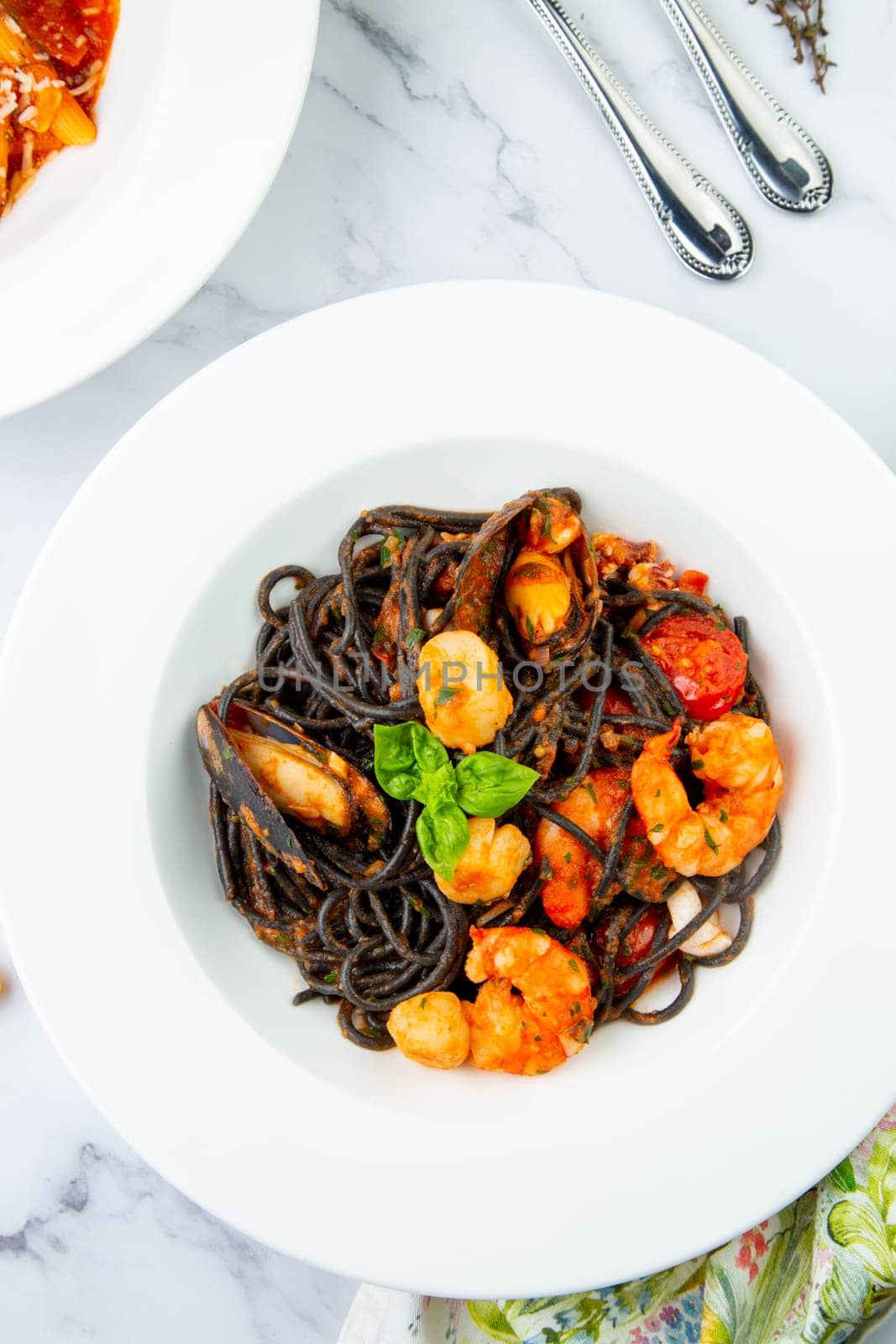 black noodles with mussels, shrimp, tomatoes and herbs side view by tewolf