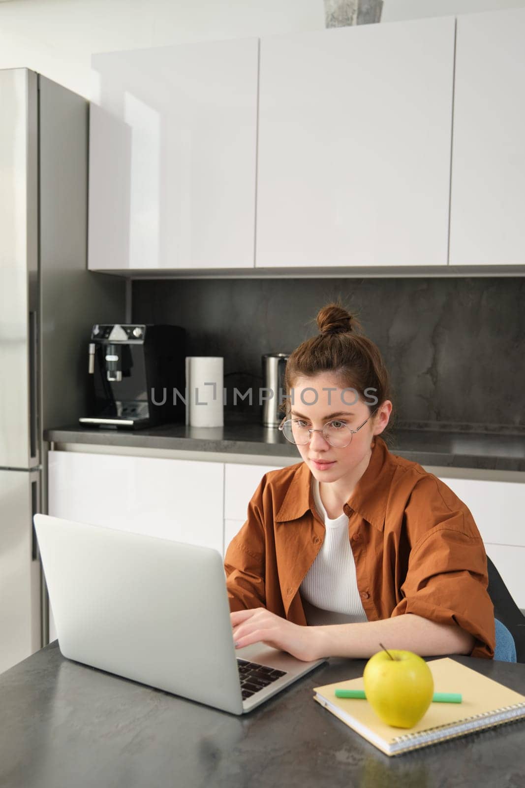 Vertical shot of young freelancer, woman working from home, typing on laptop, looking at screen.