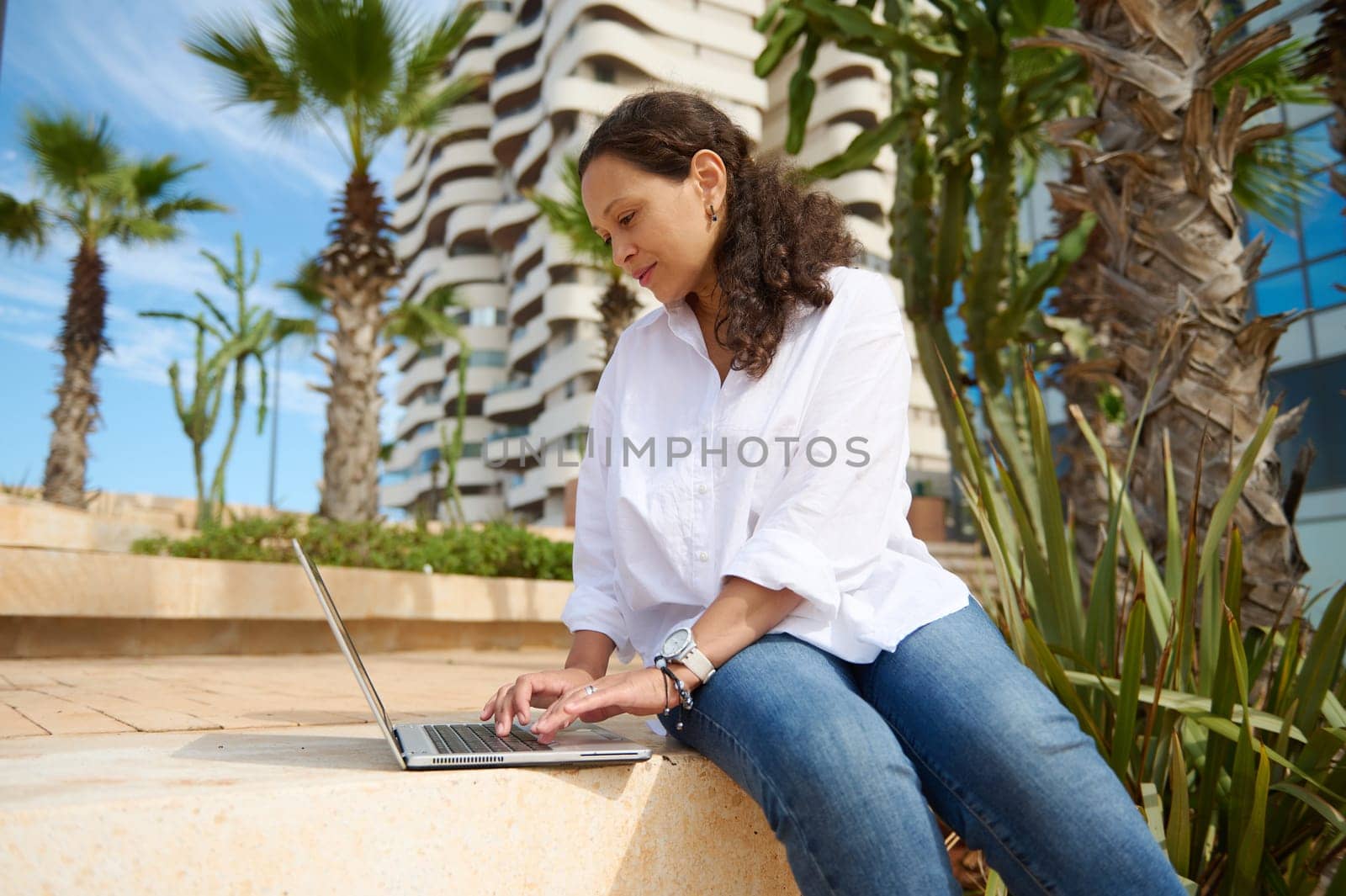 Multi-ethnic young business woman typing on laptop, working online outdoor. People. Business. Internet technology. Copy advertising text. Online education. E-learning. Remote job. Career. Recruitment