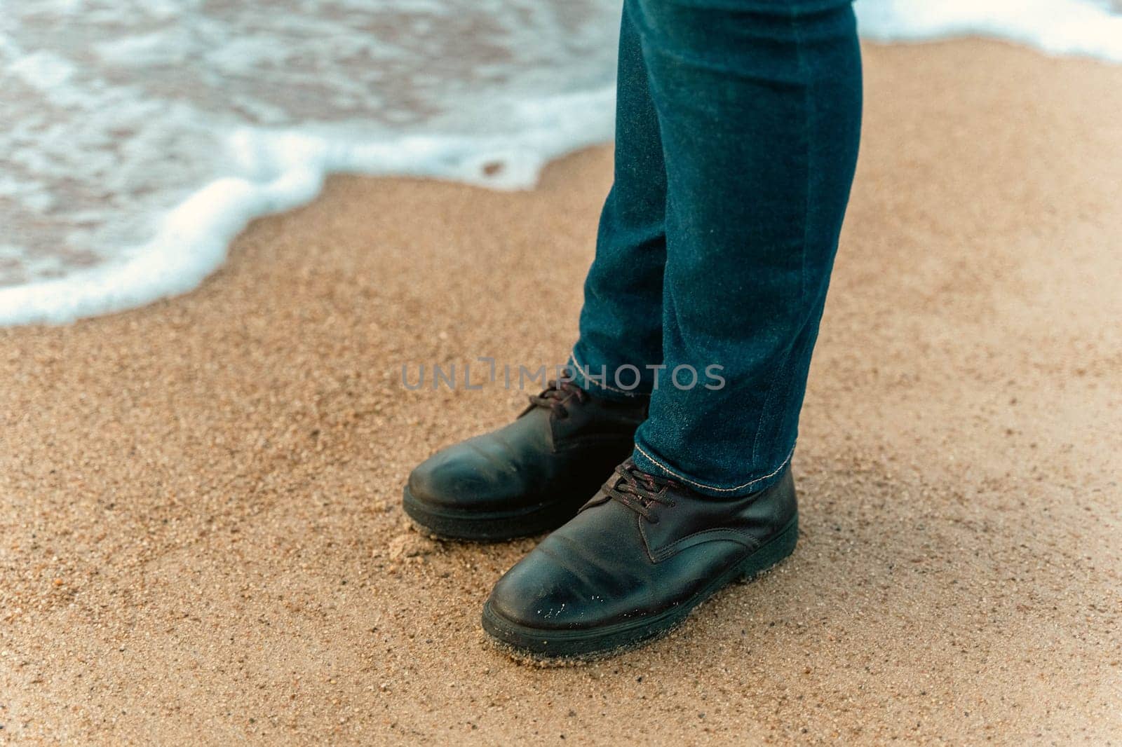 a girl walks on an autumn deserted beach. women's feet in brown leather boots on the sand of an autumn beach.