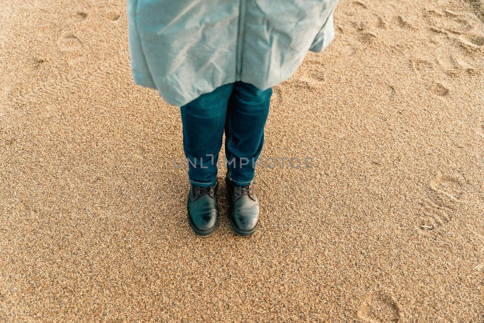 a girl walks on an autumn deserted beach. women's feet in brown leather boots on the sand of an autumn beach.