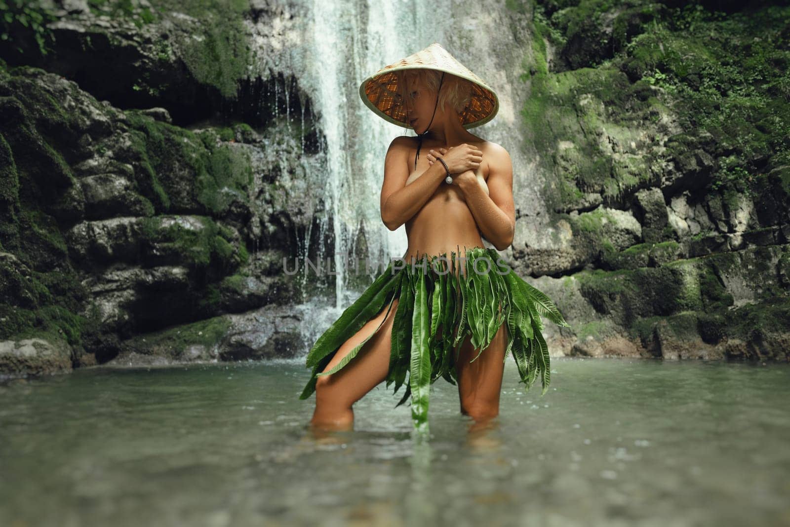 a naked sexy girl in a triangular hat and a homemade cape made of leaves stands at the waterfall of a beautiful mountain river by Rotozey