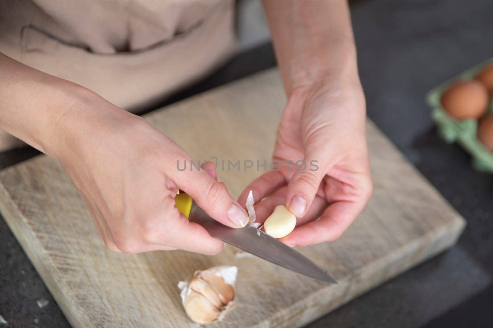 A woman cuts garlic with a knife close-up. Cutting garlic for salad or as an aromatic spice for meat. by SERSOL