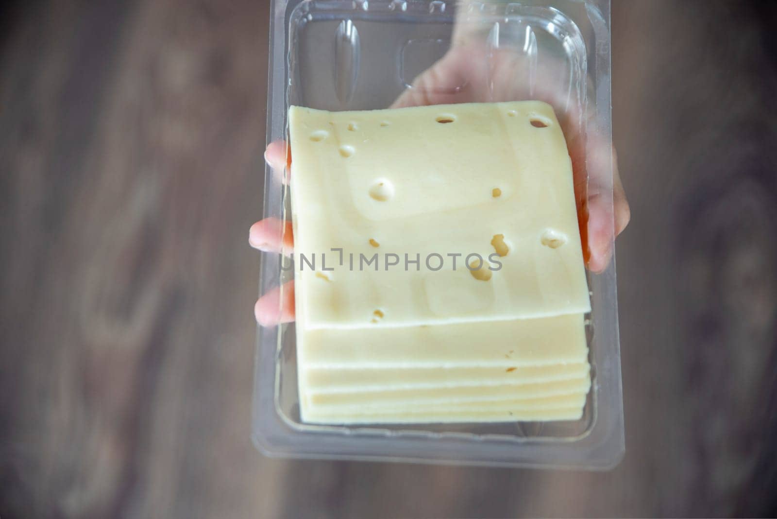 A woman's hand takes a piece of cheese from a pack close-up. Preparing for Cheese Lovers Day. by SERSOL