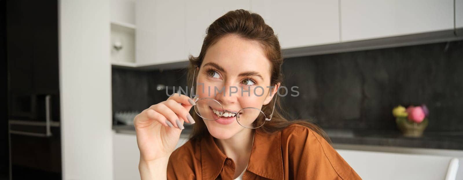 Close up portrait of carefree woman in glasses, sitting at home in kitchen, smiling and looking happy.