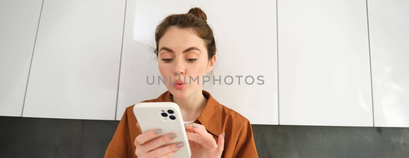 Portrait of young woman at home, looking with interest at smartphone screen, concept of online shopping, buying on mobile apps, picking something using application on phone by Benzoix
