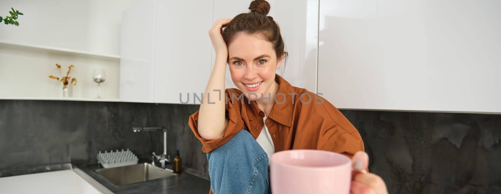 Portrait of cute young brunette woman, offering to taste her coffee, extending hand with mug of tea, smiling and looking happy.
