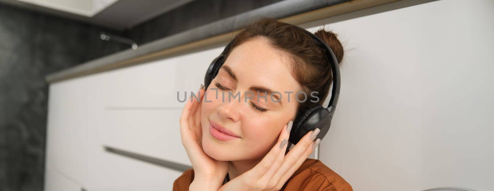 Portrait of beautiful young woman in headphones, relaxing, closes eyes from pleasure listening to music in earphones.