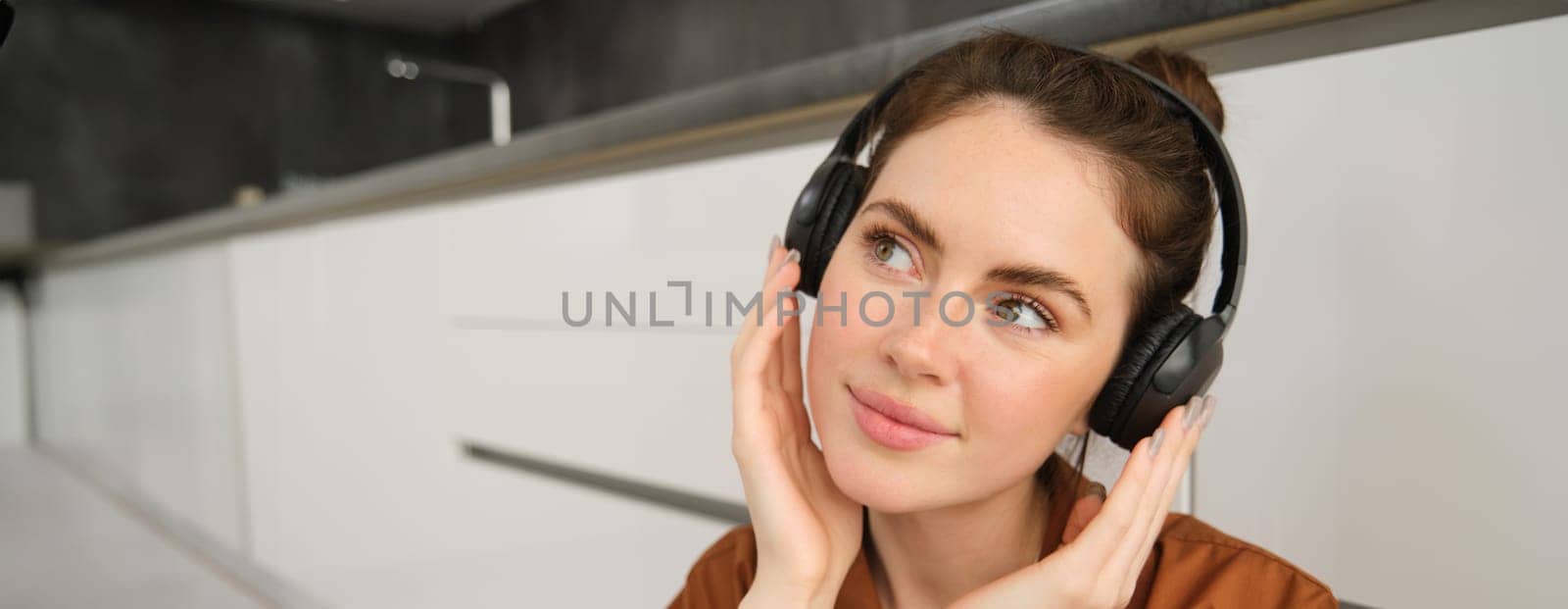 Close up portrait of happy, smiling young woman listens to music in wireless headphones, enjoys favourite song or melody in earphones.