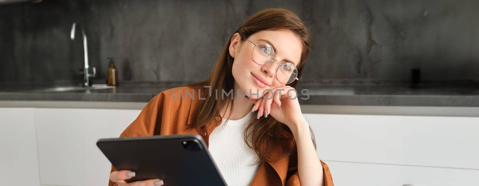 Portrait of busy young woman, self-employed entrepreneur sitting at home with digital tablet, reading documents. Student working on project remotely, holding gadget, studying.