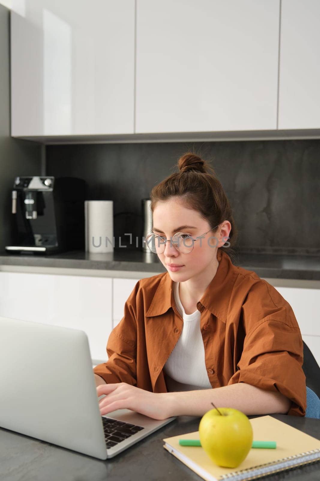 Vertical shot of woman working from home, business owner using laptop, browsing social media on computer, wearing glasses.