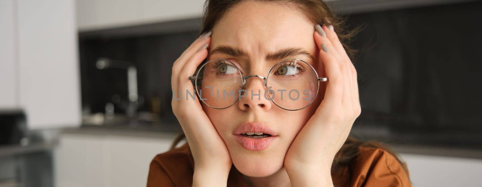 Portrait of woman thinking about something concerning, wearing glasses, touching head, sitting troubled at home.