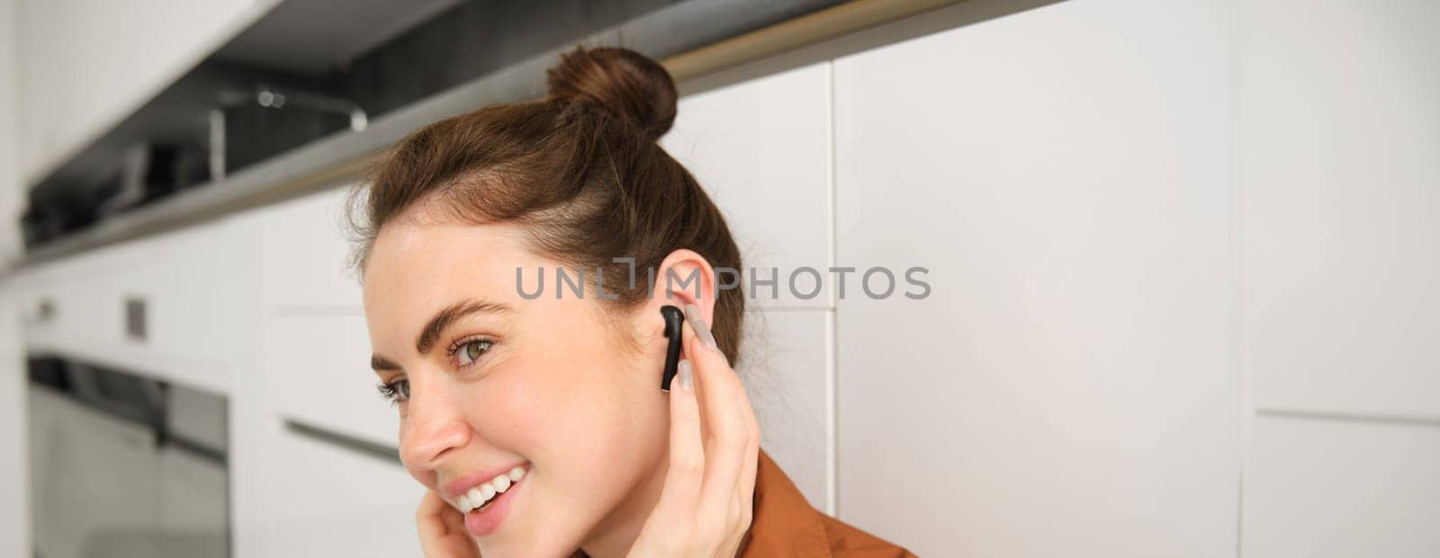 Close up portrait of girl enjoying listening to music in wireless earphones, smiling, wearing headphones, sitting at home by Benzoix