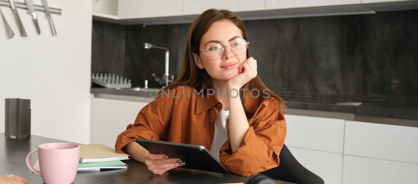 Portrait of young woman working from home, connecting to lesson on digital tablet, reading in glasses, studying remotely in her kitchen, distance learning and education concept.