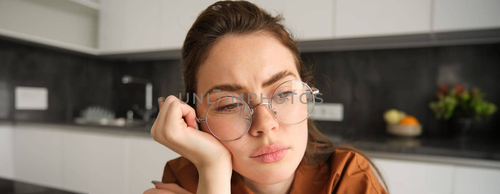 Close up portrait of woman in glasses with concerned, sad face, looking upset, troubled expression, sitting at home.