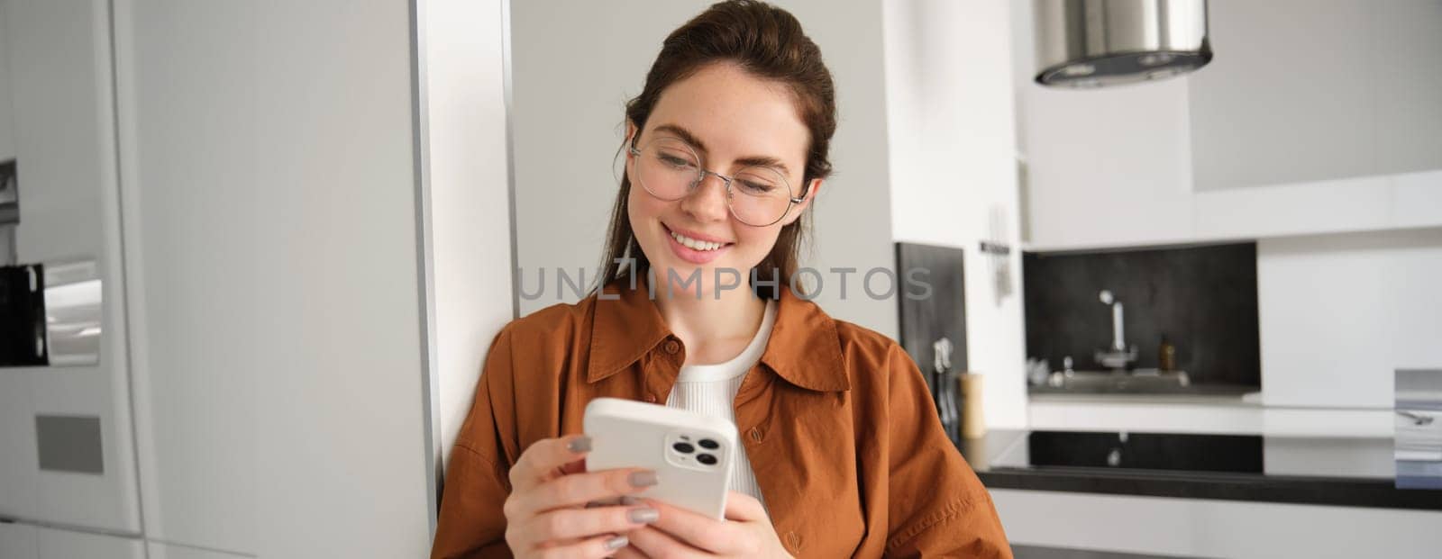 Beautiful woman checking social media while using smartphone at home. Smiling young female using mobile phone app and playing game, shopping online or reading news. Copy space by Benzoix