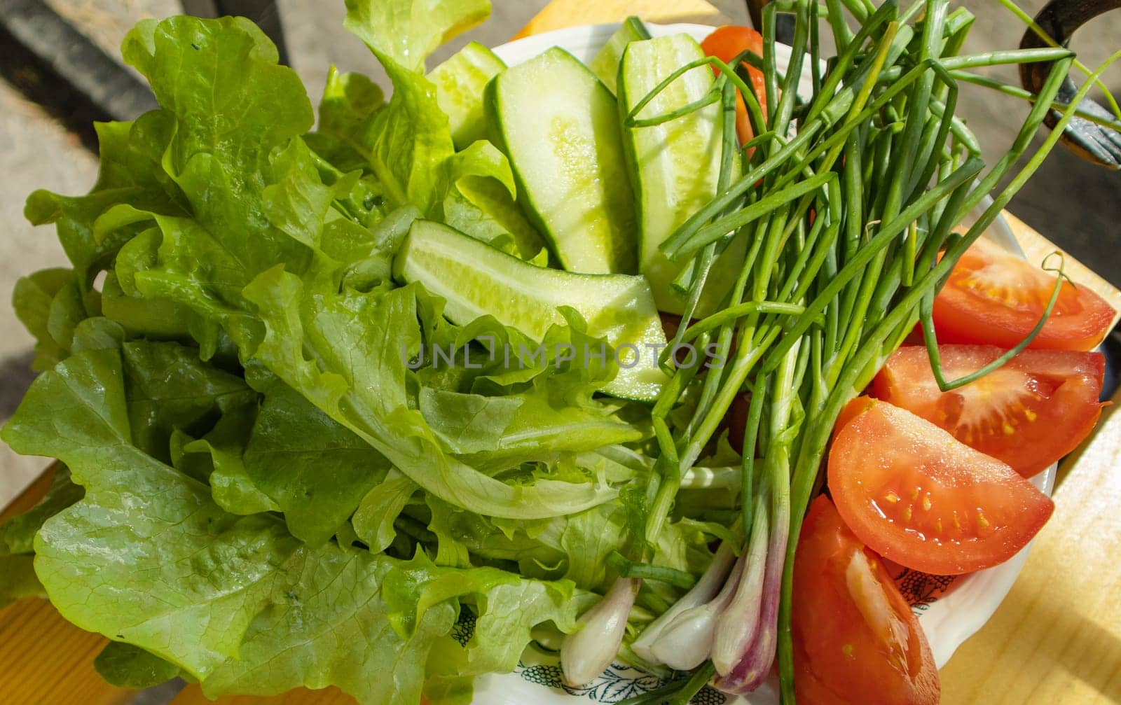 Fresh vegetables - lettuce, green onion, tomatoes and cucumbers on a white plate on a wooden background. The concept of cooking healthy food. View from above.
