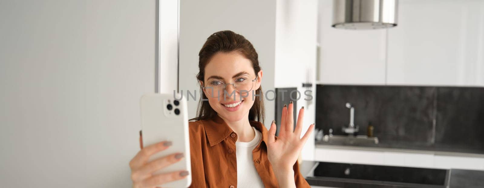 Portrait of stylish beautiful woman at home, video chats on smartphone, connects to online meeting from her living room, lifestyle social media blogger records a video on mobile phone by Benzoix