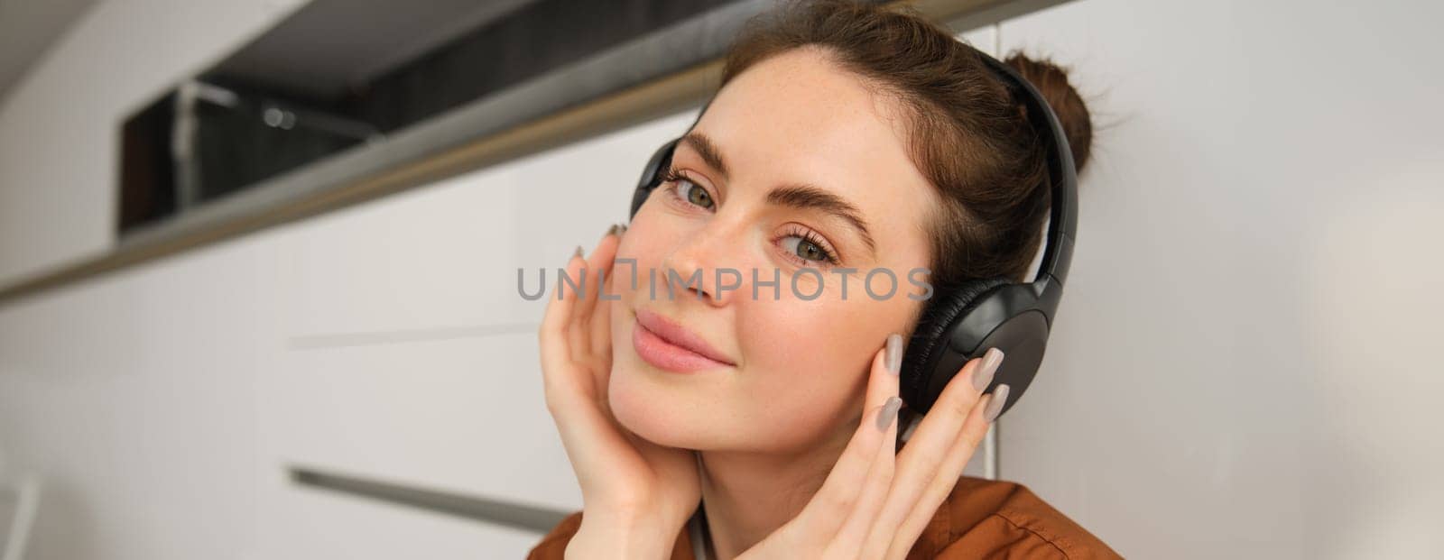 Portrait of smiling woman with headphones, listens to music, looks at camera by Benzoix